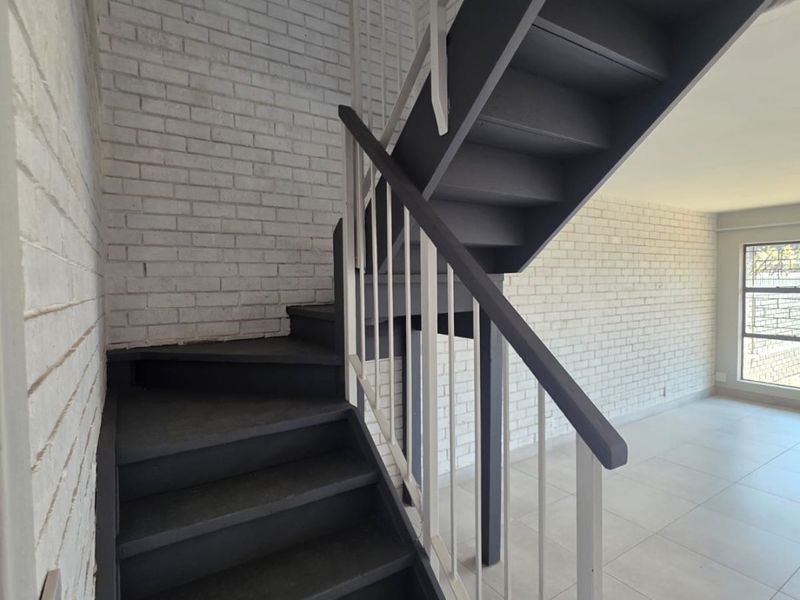 A bright, modern hallway featuring a painted staircase with a metal balustrade, white brick-style walls, and neutral floor tiles.