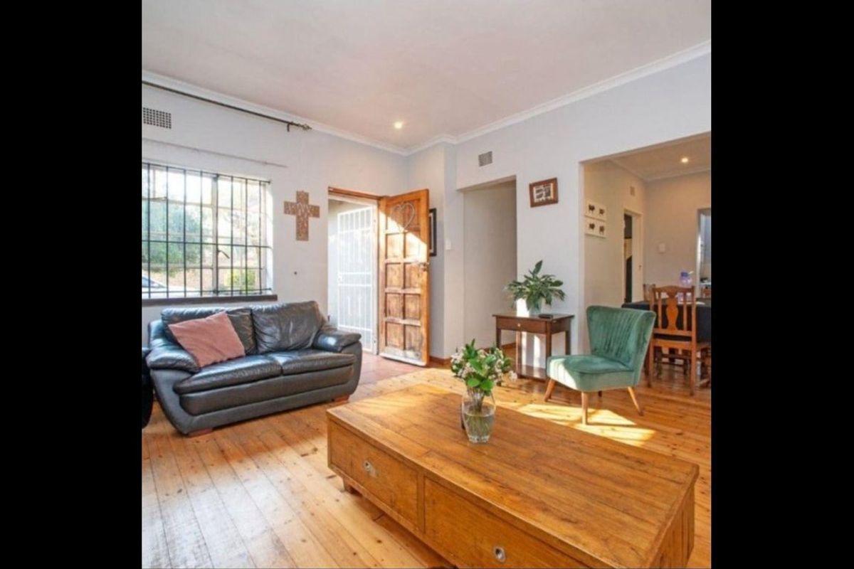 A bright living room featuring polished timber flooring, recessed lighting, and a solid timber entrance door with security bars on the window.