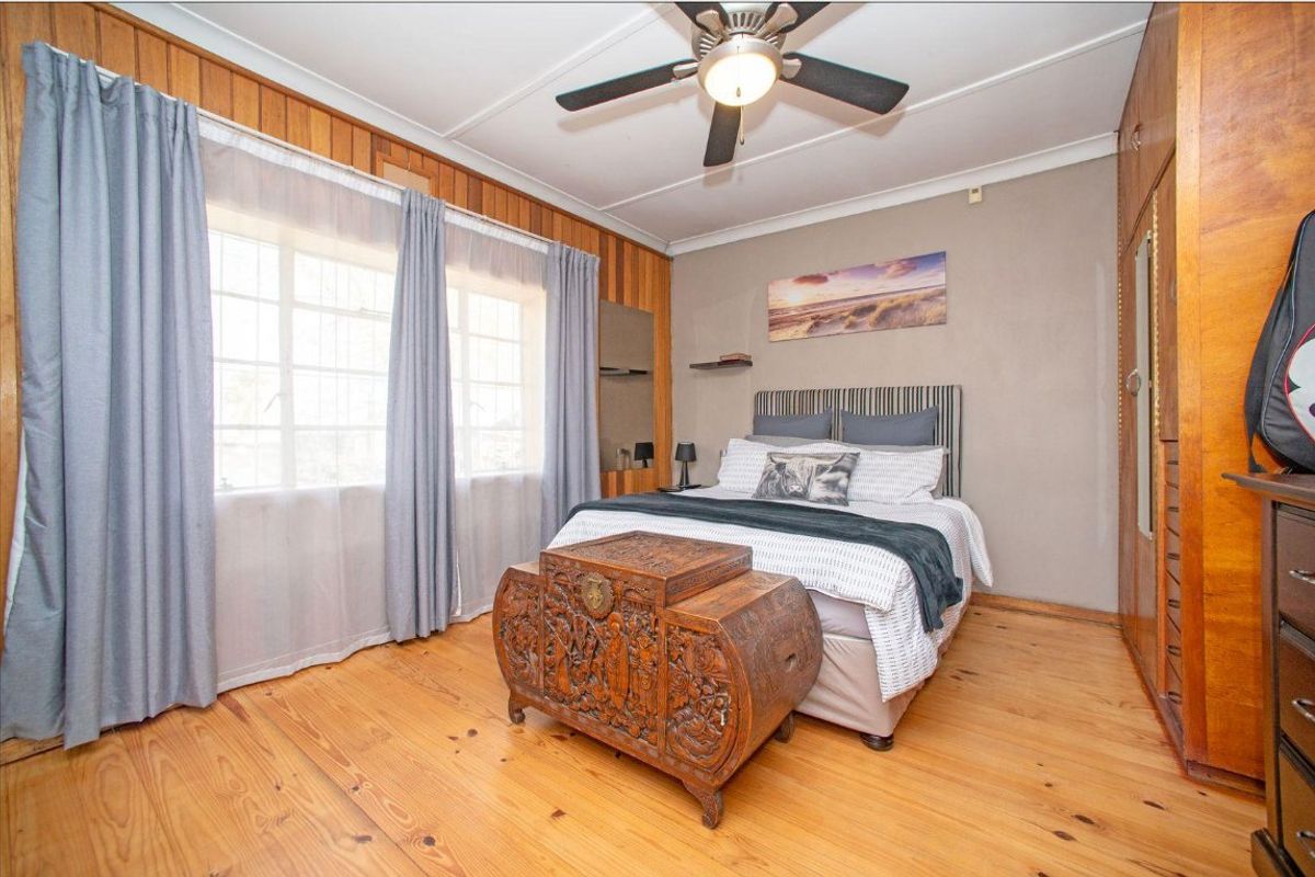 A bedroom featuring timber wall paneling, polished timber flooring, a ceiling fan, and built-in storage cupboards.