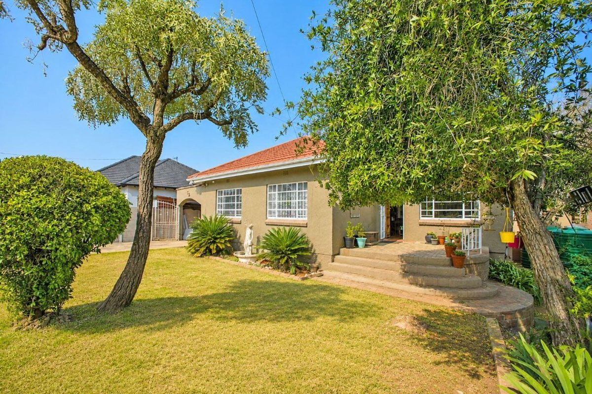 Rear view of the house featuring a landscaped garden, brick patio with concrete steps, and secure window bars.