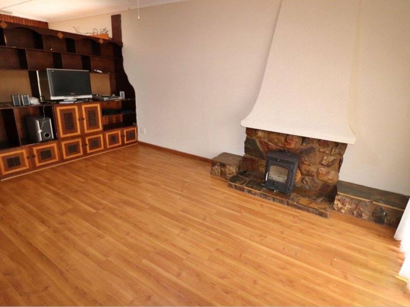 Living room featuring a prominent stone fireplace with a wood-burning stove and a large built-in wooden shelving unit, finished with laminate flooring.