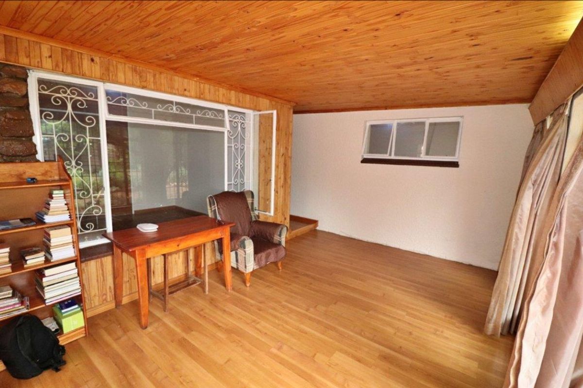A living area featuring timber ceiling and wall paneling, laminate flooring, and large windows with security gates.