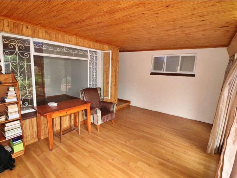 A living area featuring timber ceiling and wall paneling, laminate flooring, and large windows with security gates.
