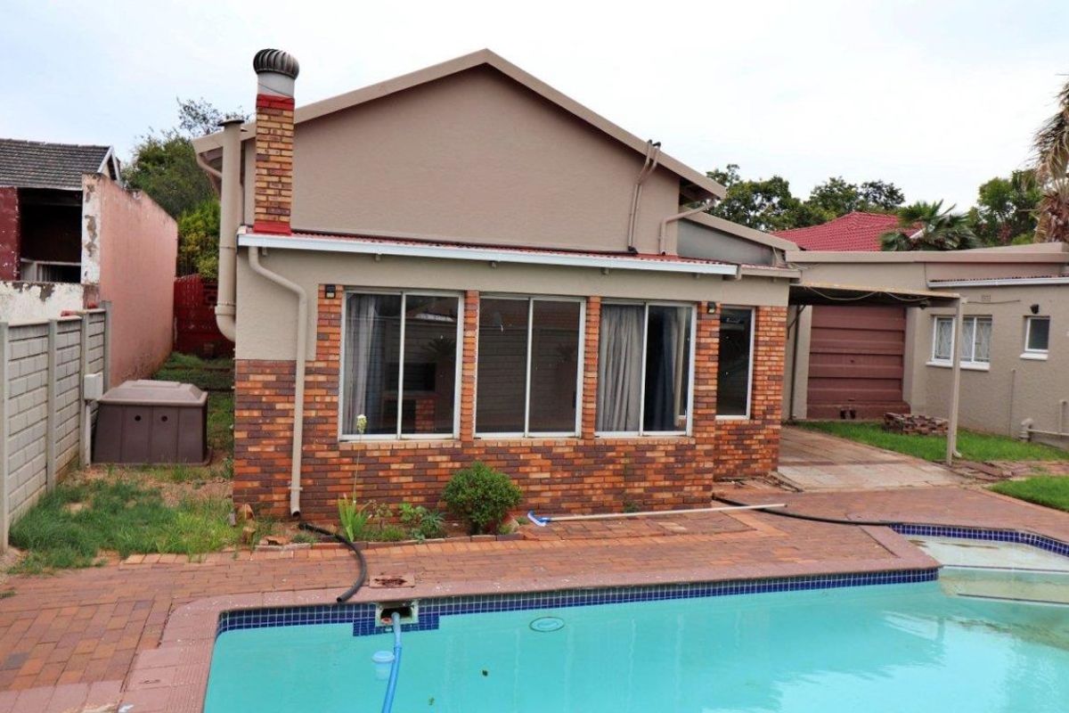 Rear view of the property featuring a swimming pool, paved patio area, and brick facade with sliding windows.