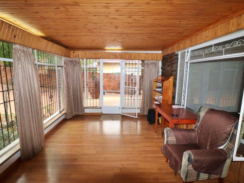 Enclosed patio area featuring timber ceiling, laminate flooring, and large windows with security gates, offering a bright and versatile space.