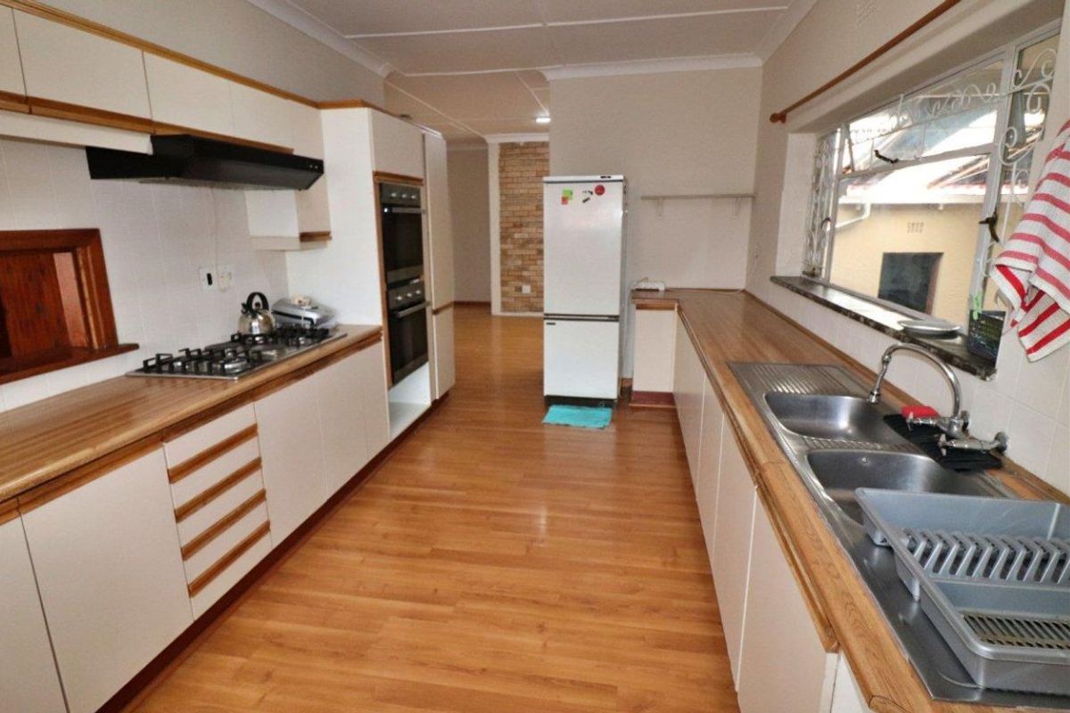 A functional galley-style kitchen featuring white cabinetry, wood-look laminate countertops, a gas hob, double wall oven, and double stainless steel sink.