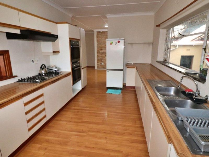 A functional galley-style kitchen featuring white cabinetry, wood-look laminate countertops, a gas hob, double wall oven, and double stainless steel sink.