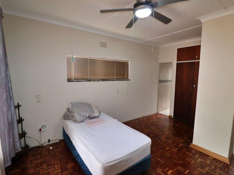 A bedroom featuring classic parquet flooring, a ceiling fan, and built-in storage cupboards, offering a functional and well-maintained living space.
