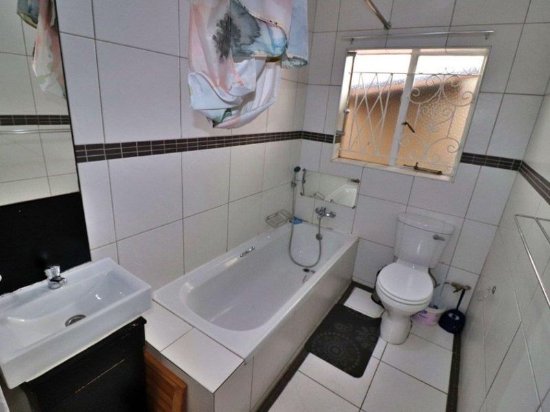 A functional bathroom featuring a built-in bathtub, wall-mounted basin, toilet, and tiled finishes throughout.