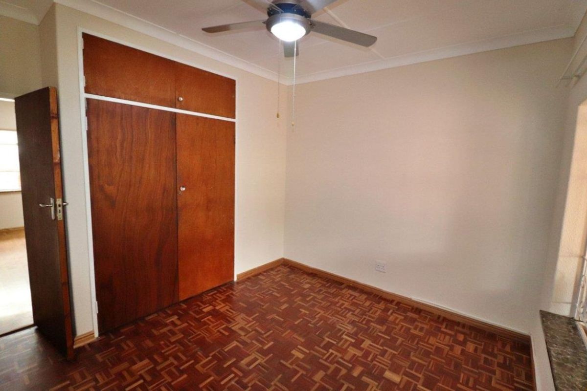 An empty bedroom featuring classic parquet flooring, built-in wooden cupboards, and a ceiling fan, offering a blank canvas for personalization.