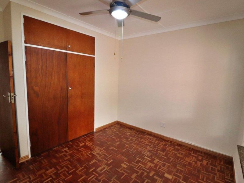 An empty bedroom featuring classic parquet flooring, built-in wooden cupboards, and a ceiling fan, offering a blank canvas for personalization.