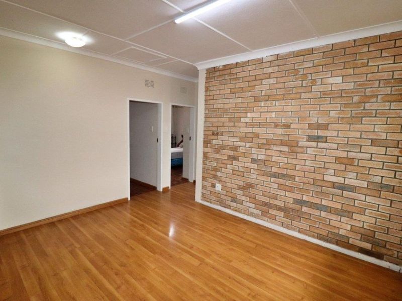 An empty living room featuring a prominent exposed brick feature wall, laminate flooring, and dual ceiling lighting fixtures.