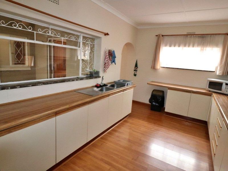 Functional kitchen featuring laminate cabinetry, wooden countertops, a double bowl sink, and built-in hob, with security bars on the window.