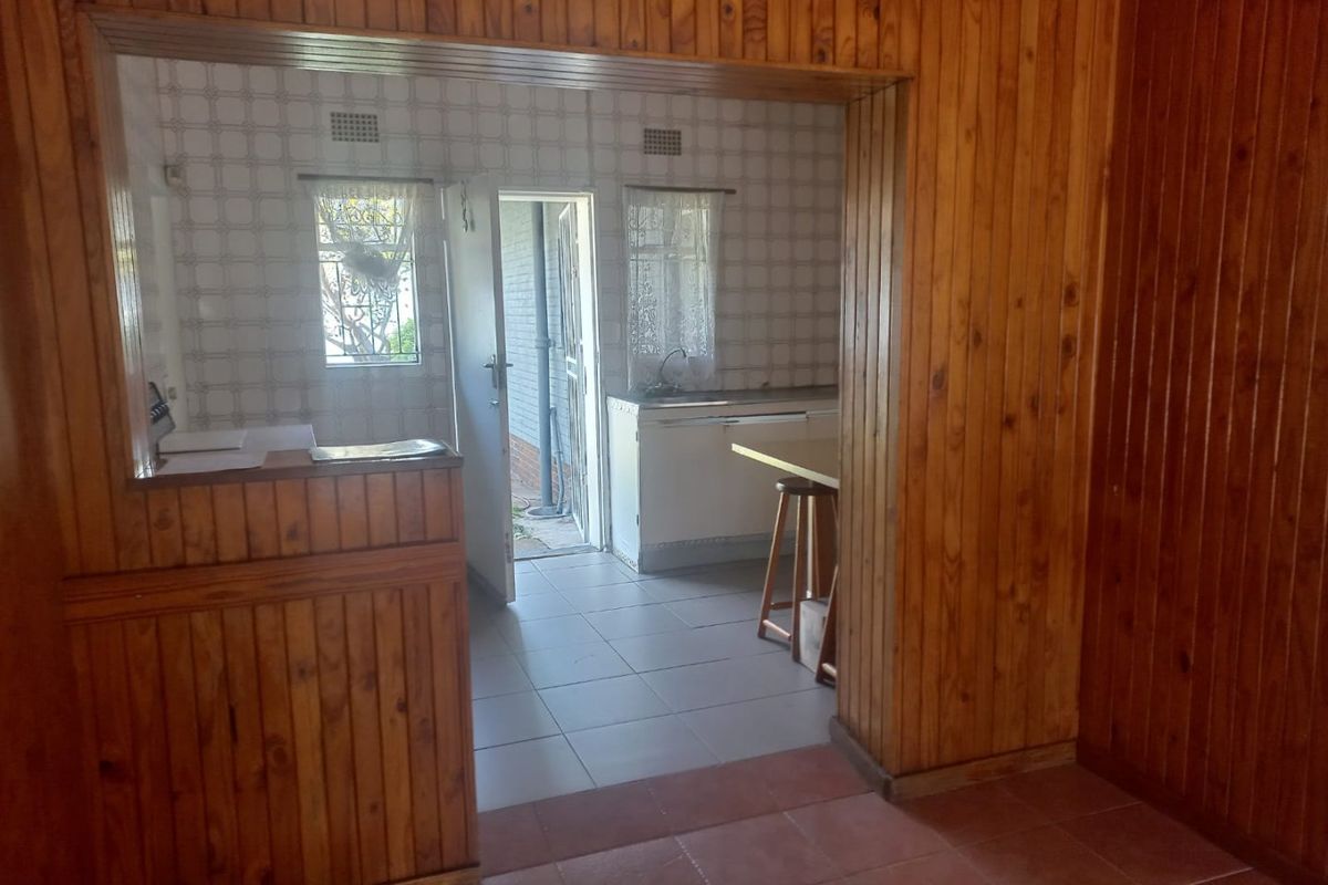 A dated kitchen area featuring extensive wooden wall paneling, tiled flooring, and direct access to the exterior through a security door.