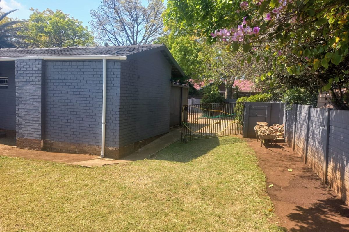 A view of the rear garden featuring a painted brick exterior wall, tiled roof, and a secure metal gate leading to the backyard area.