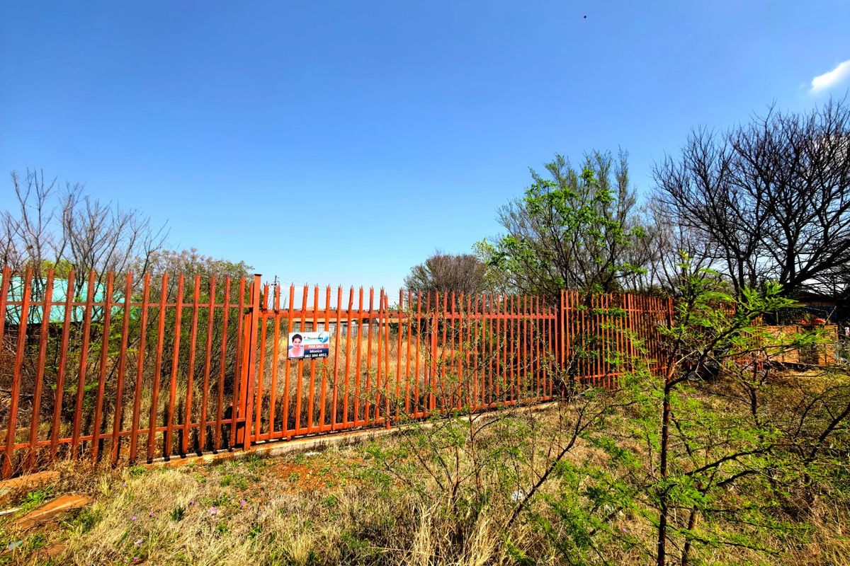 A vacant residential plot secured by steel palisade fencing with a concrete plinth, showing signs of surface rust.