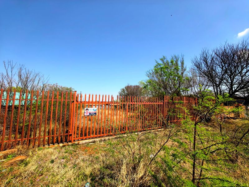 A vacant residential plot secured by steel palisade fencing with a concrete plinth, showing signs of surface rust.