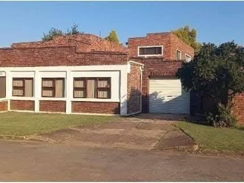 Front exterior view of a single-story brick house featuring a driveway, attached garage, and surrounding boundary wall.
