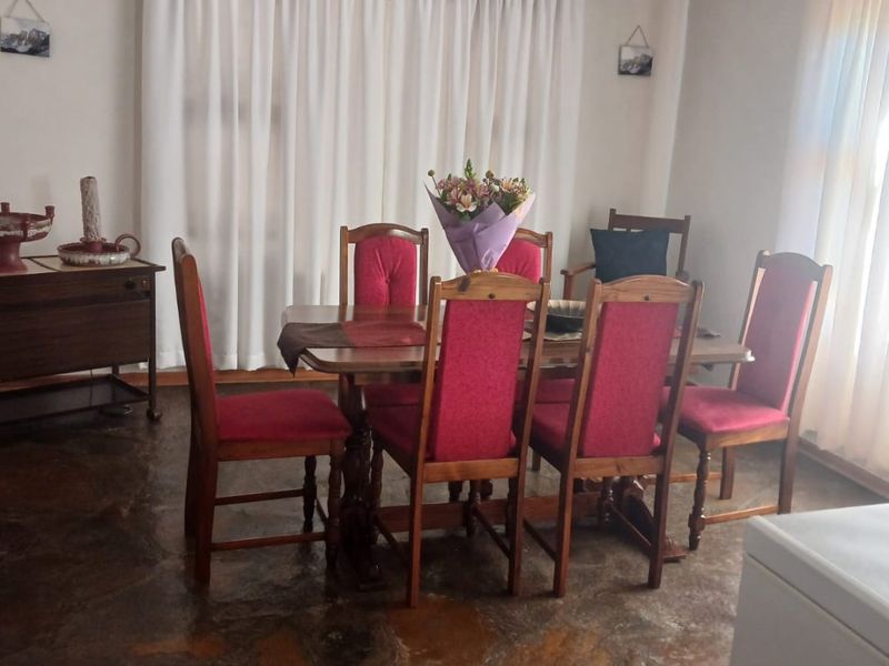 A dining room featuring rustic stone flooring, neutral walls, and natural light provided by large windows with curtains.