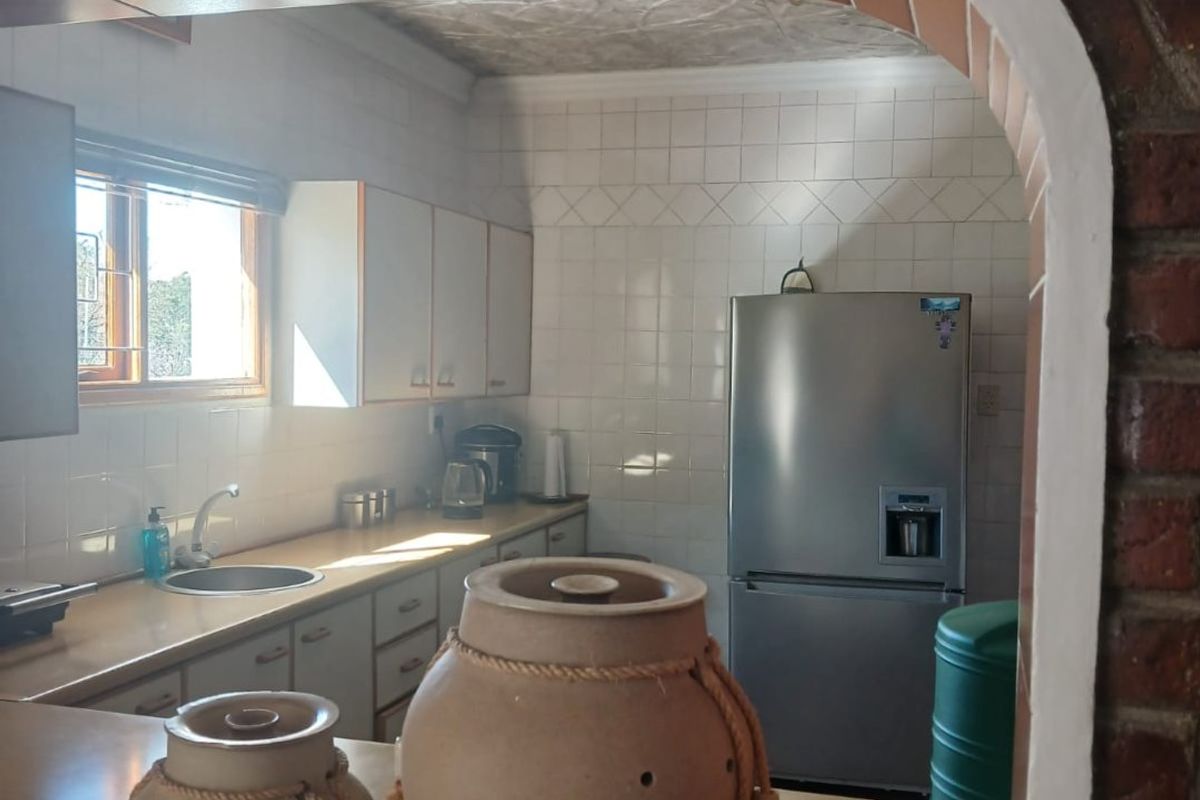 A functional kitchen featuring white cabinetry, tiled splashbacks, and a distinctive exposed brick archway serving as a pass-through to the adjacent living area.