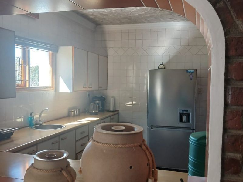A functional kitchen featuring white cabinetry, tiled splashbacks, and a distinctive exposed brick archway serving as a pass-through to the adjacent living area.