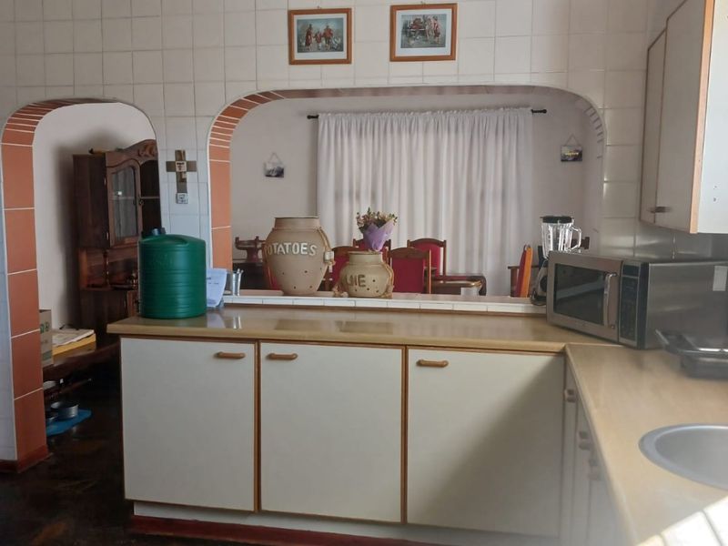A dated kitchen featuring laminate countertops, tiled splashbacks, and stone flooring, with an open archway connecting to the adjacent living area.