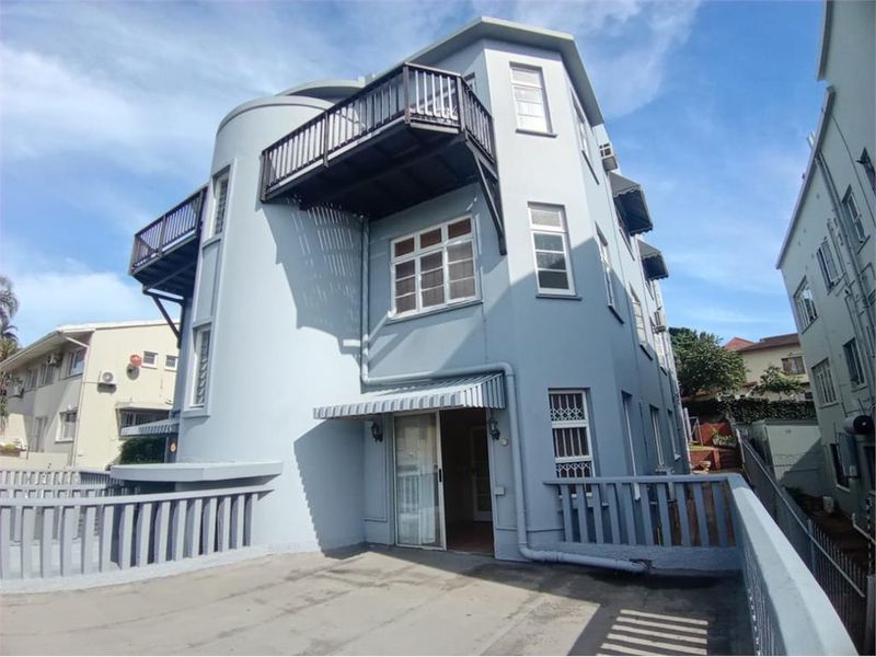 Rear exterior view of the apartment building featuring multiple balconies, sliding glass doors, and protective awnings with a paved outdoor area.