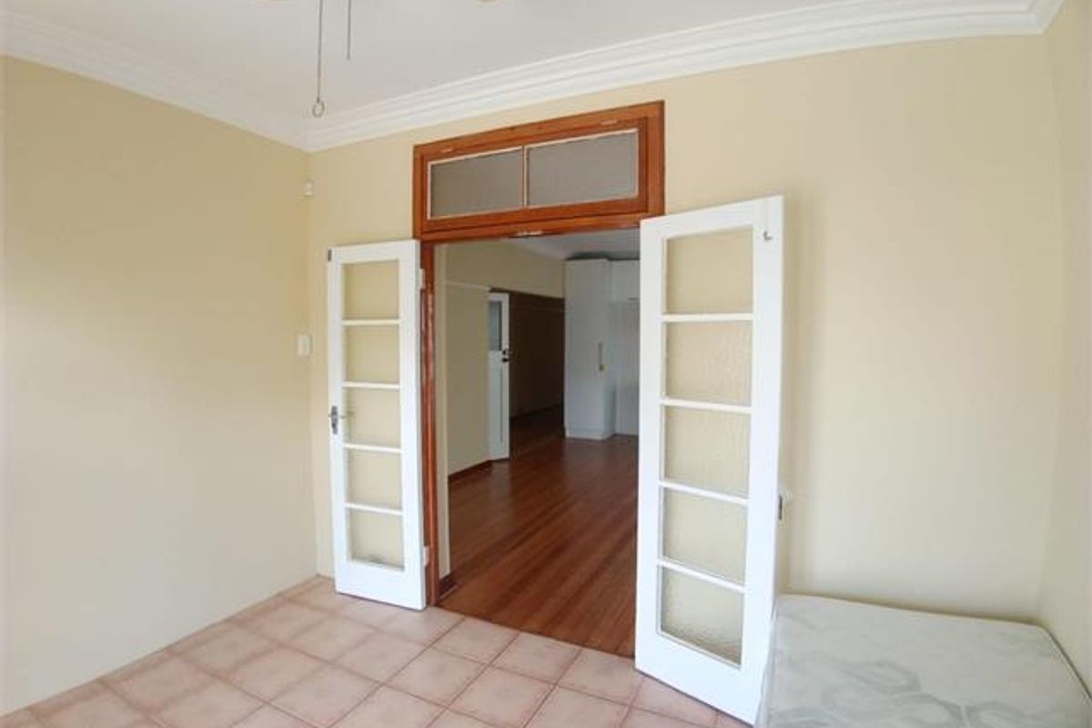 A bright living area featuring tiled floors, crown molding, a ceiling fan, and classic French doors opening into an adjacent room with hardwood flooring.