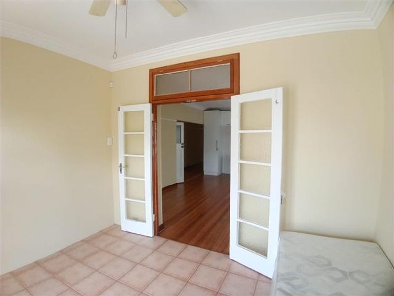 A bright living area featuring tiled floors, crown molding, a ceiling fan, and classic French doors opening into an adjacent room with hardwood flooring.