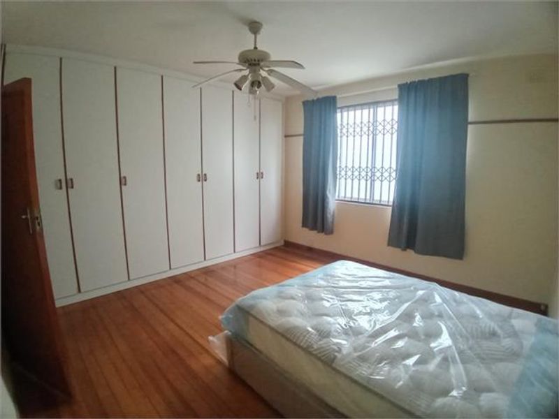 A bedroom featuring hardwood flooring, extensive built-in cupboards, a ceiling fan, and a window fitted with a security gate.
