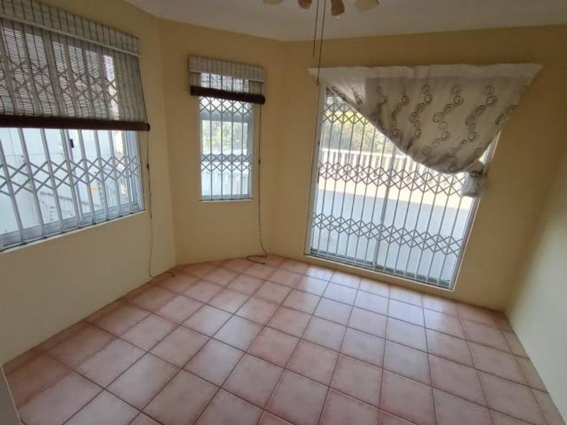 An empty living area featuring tiled flooring, security gates on windows and sliding doors, and a ceiling fan, offering a blank canvas for renovation.