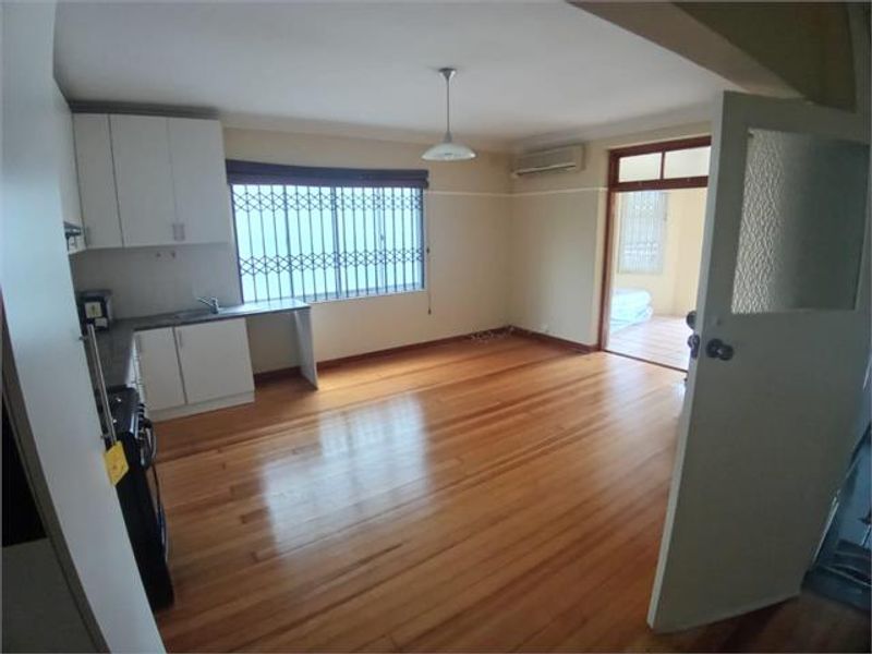 An open-plan living and kitchen area featuring polished hardwood floors, built-in cabinetry, and a security-fitted window, offering a functional and versatile living space.