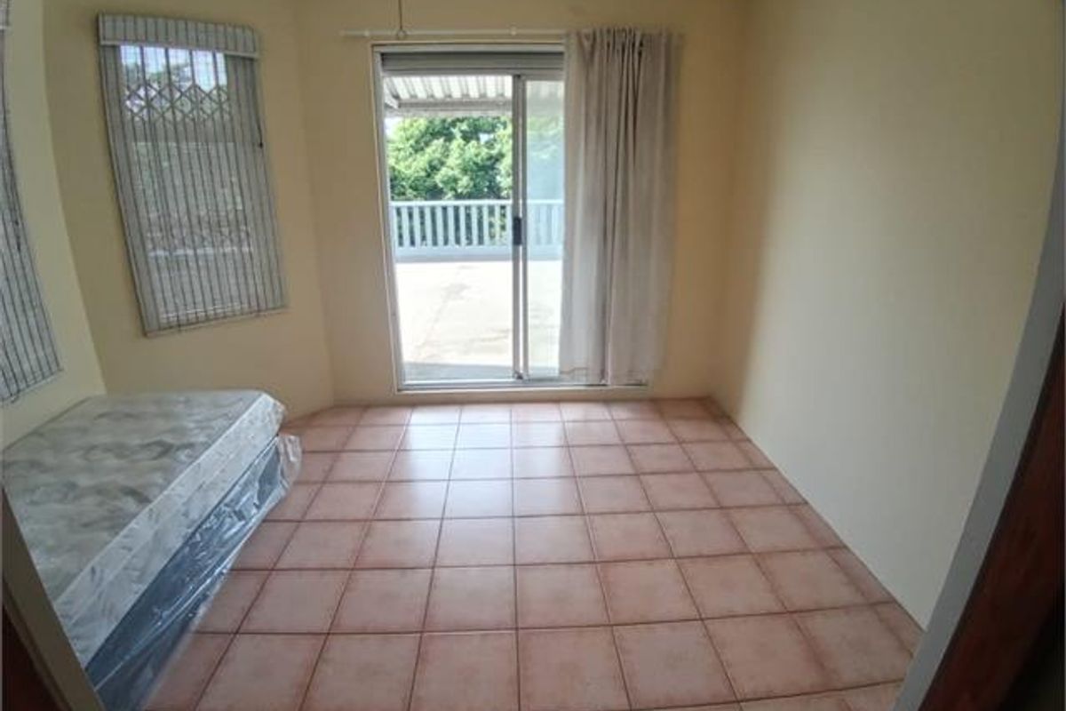 A vacant bedroom featuring ceramic floor tiles, sliding glass doors leading to a balcony, and security window treatments.