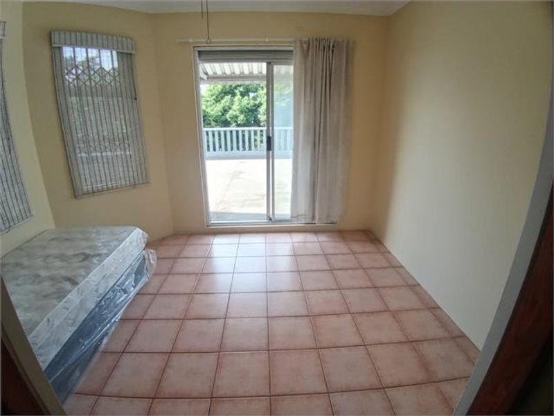 A vacant bedroom featuring ceramic floor tiles, sliding glass doors leading to a balcony, and security window treatments.
