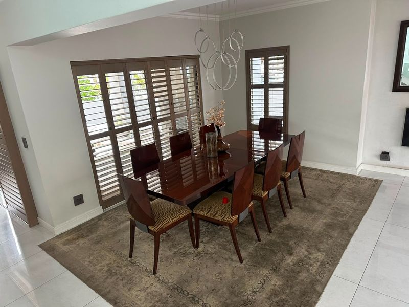 A bright dining room featuring tiled flooring, modern pendant lighting, and plantation shutters providing natural light control.