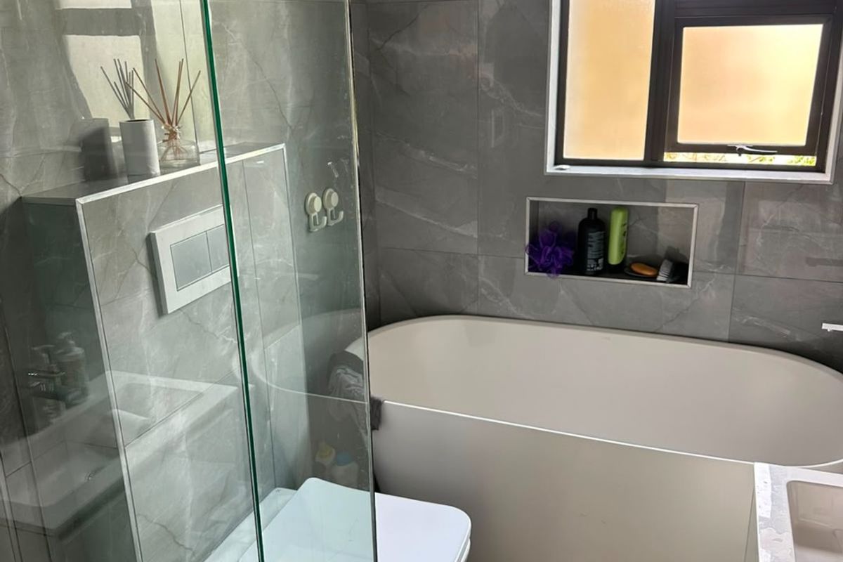 Modern bathroom featuring a freestanding bathtub, glass-enclosed shower, wall-mounted toilet, and sleek grey porcelain tiling with a convenient recessed storage niche.
