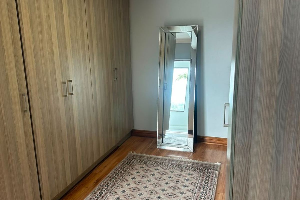A well-maintained bedroom featuring extensive built-in timber-finish wardrobes, warm timber flooring, and classic cove cornice detailing.