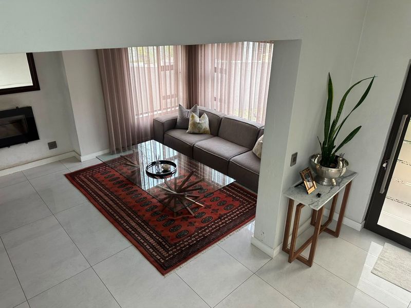 A bright living room featuring large windows with vertical blinds, tiled flooring, and a built-in fireplace, offering a clean and well-maintained living space.
