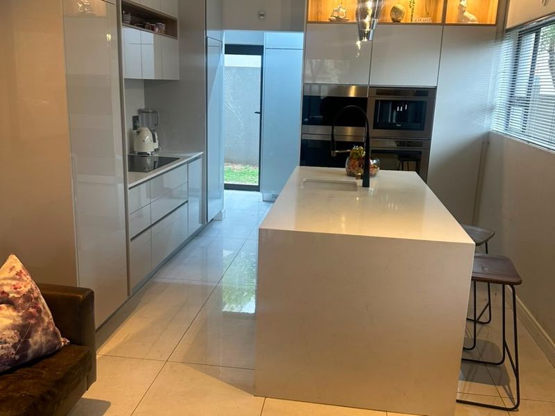 Modern kitchen featuring high-gloss cabinetry, a large central island with quartz countertops, built-in appliances, and sleek tiled flooring.