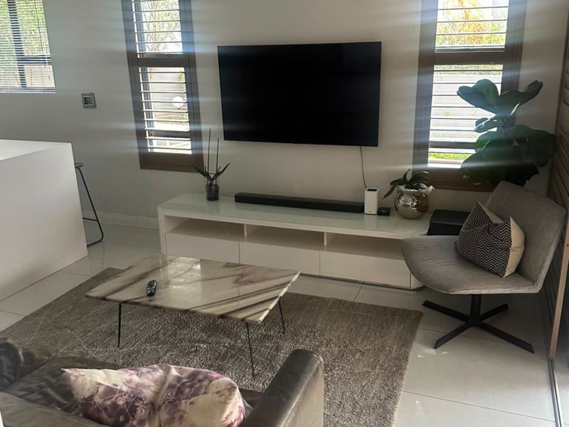 A bright living room featuring tiled flooring, plantation shutters on the windows, and recessed downlighting, creating a clean and modern atmosphere.