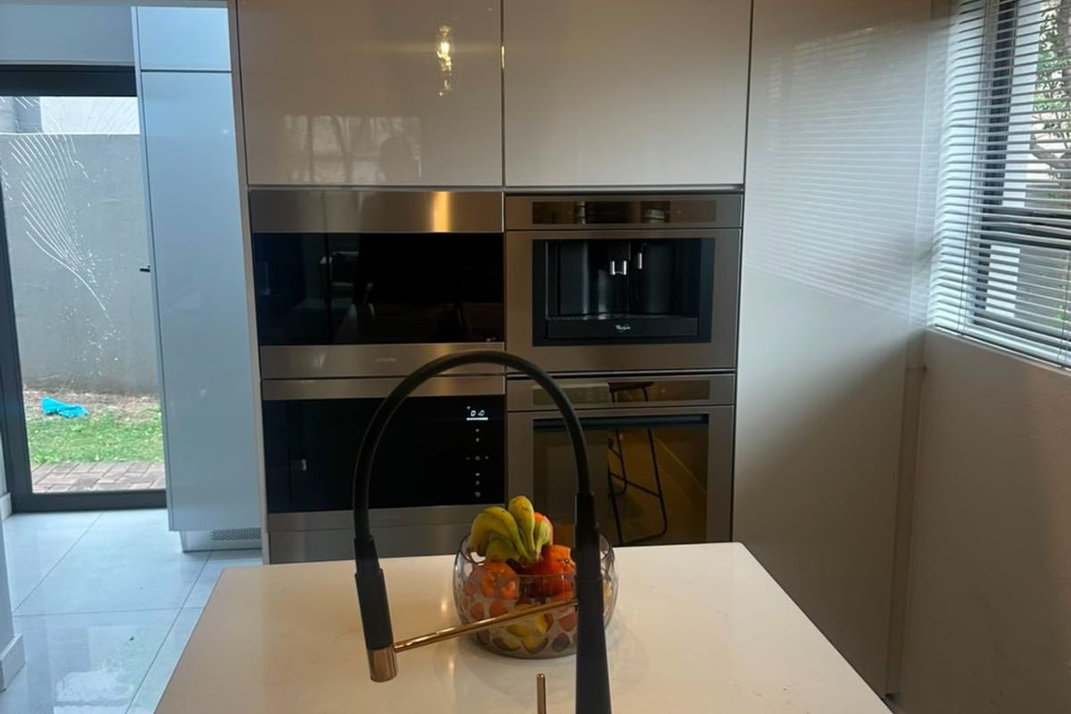 Modern kitchen featuring high-gloss cabinetry, integrated appliances including a coffee machine and oven, a central island with quartz countertop, and a stylish gooseneck faucet.