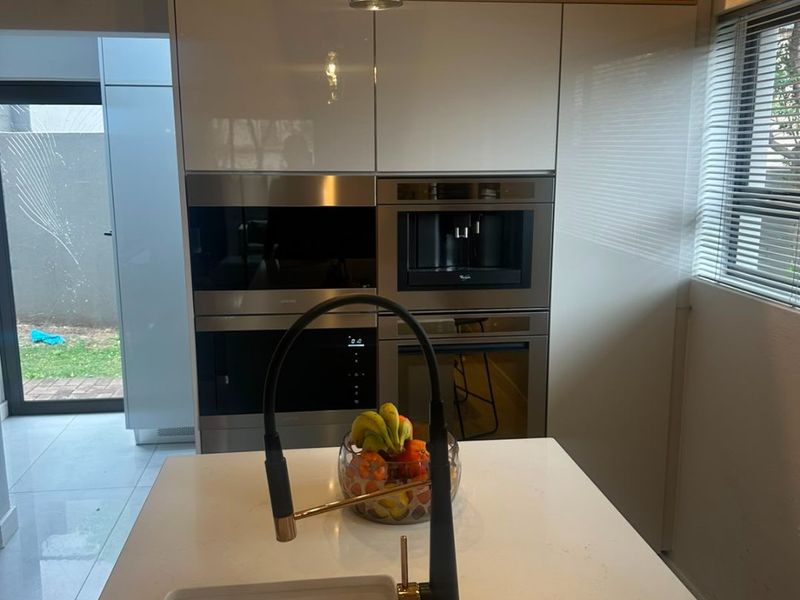 Modern kitchen featuring high-gloss cabinetry, integrated appliances including a coffee machine and oven, a central island with quartz countertop, and a stylish gooseneck faucet.