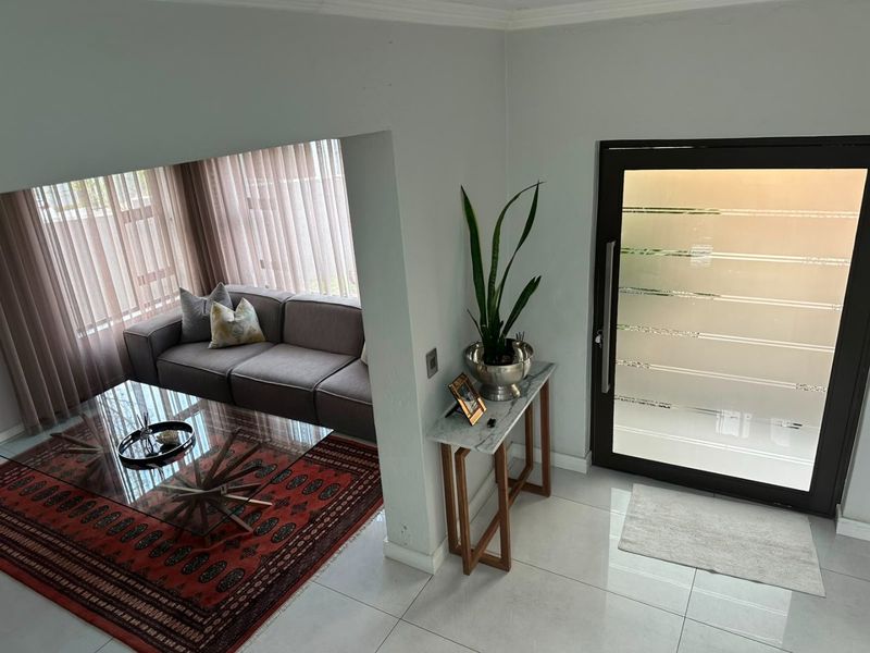 A bright entrance hall featuring modern tiled flooring and a contemporary frosted glass front door, leading into an adjacent living area.