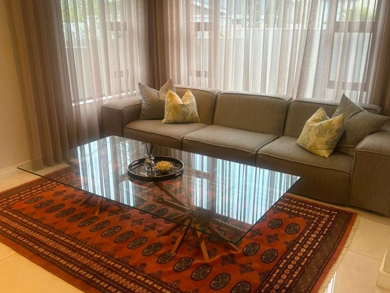 A bright and well-maintained living room featuring large windows with floor-to-ceiling curtains, recessed downlighting, and polished tiled flooring.
