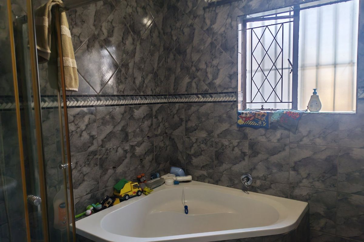 A bathroom featuring a corner bathtub, shower enclosure, and full-height marble-effect wall tiling with decorative border accents.