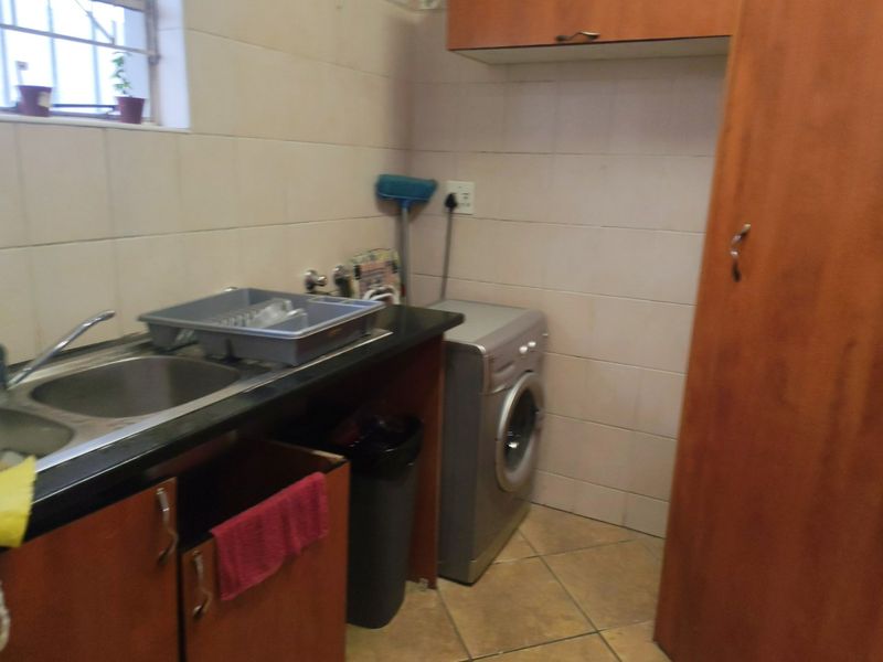 A functional laundry area featuring tiled walls, laminate cabinetry, a double sink, and space for a washing machine.