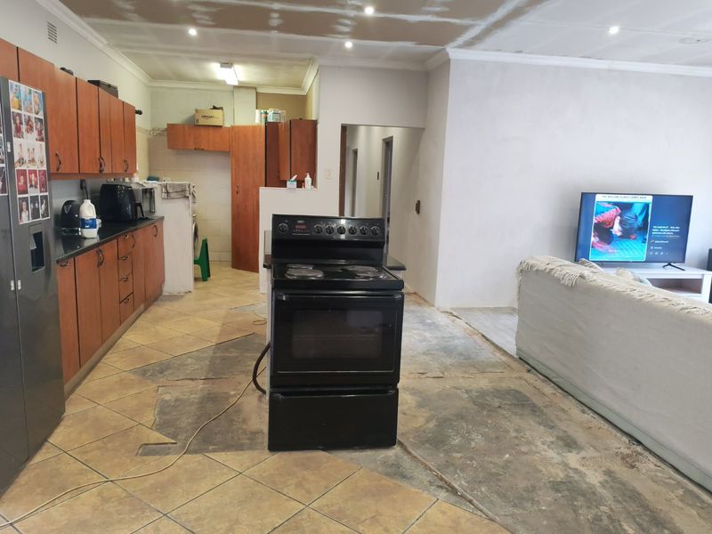 Open plan kitchen and living area featuring wooden cabinetry and a freestanding stove, currently undergoing renovation with unfinished ceiling and flooring.