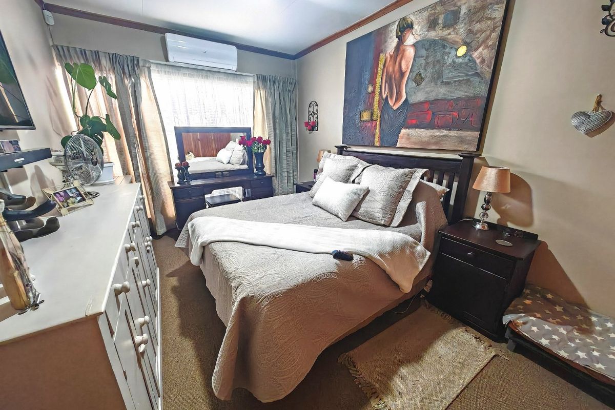 A cozy bedroom featuring carpeted flooring, a wall-mounted split-system air conditioner, and neutral wall finishes, providing a comfortable and functional sleeping space.
