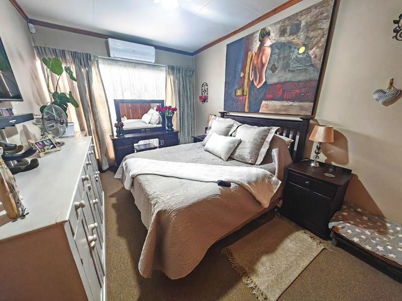 A cozy bedroom featuring carpeted flooring, a wall-mounted split-system air conditioner, and neutral wall finishes, providing a comfortable and functional sleeping space.