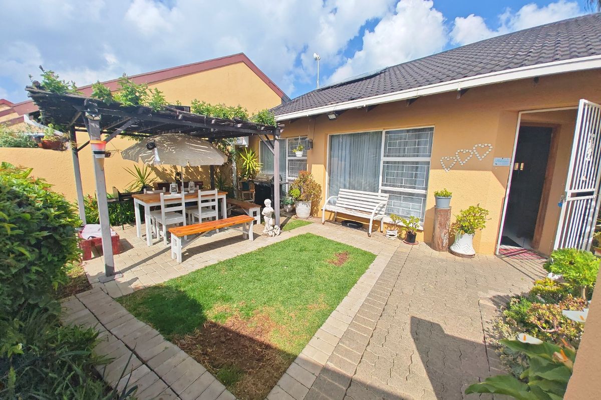 A private rear courtyard featuring a paved patio area, a timber pergola, and a small central lawn section.